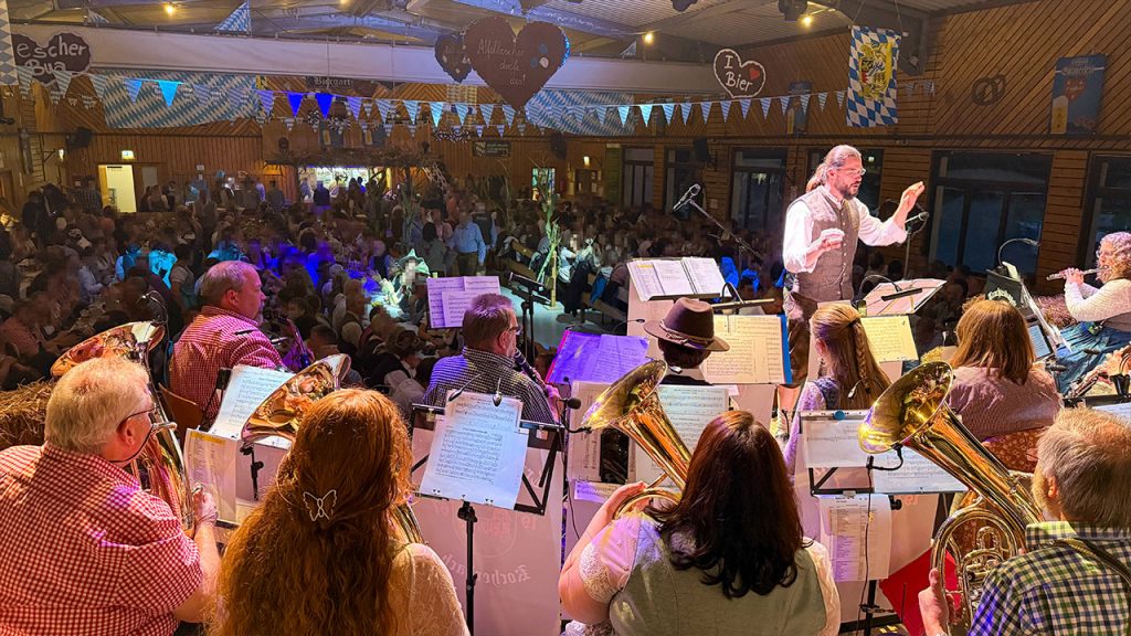 Blick von der Bühne - Sebastian Schertel beim Dirigieren im gelblichen Licht - im Hintergrund das Publikum